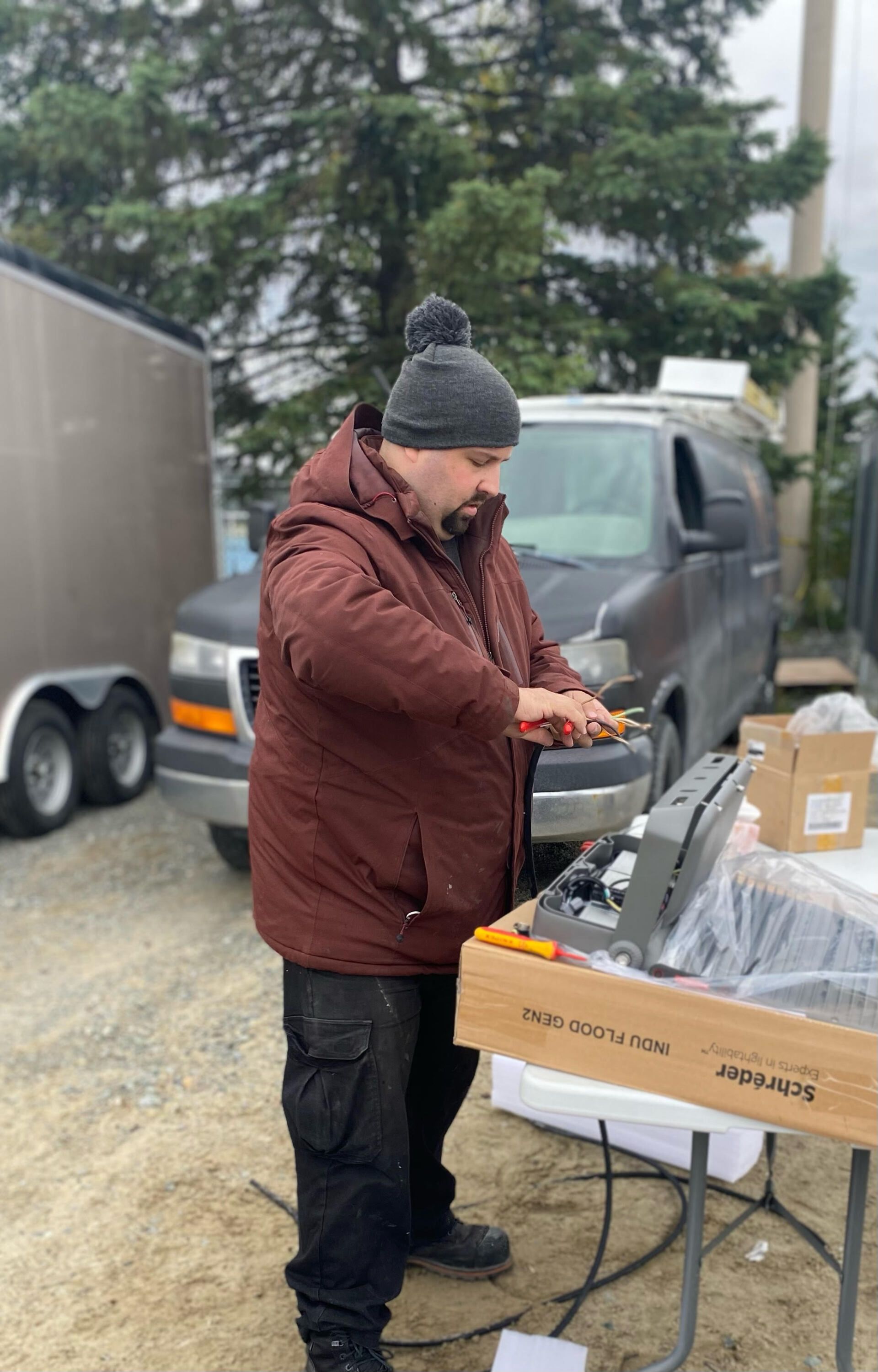 Un homme se tient devant une camionnette en train de couper des fils.