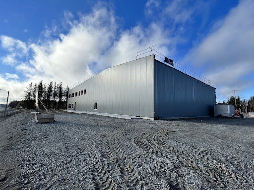 Un grand bâtiment gris se trouve au sommet d'un champ de terre.