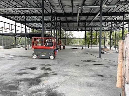 Un chantier de construction avec une nacelle élévatrice à ciseaux rouge au milieu.