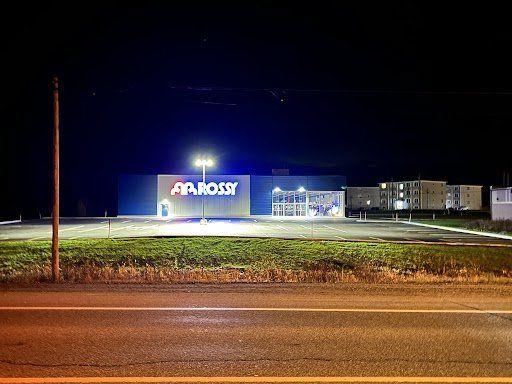 Un grand bâtiment avec le mot Rossy dessus est éclairé la nuit.