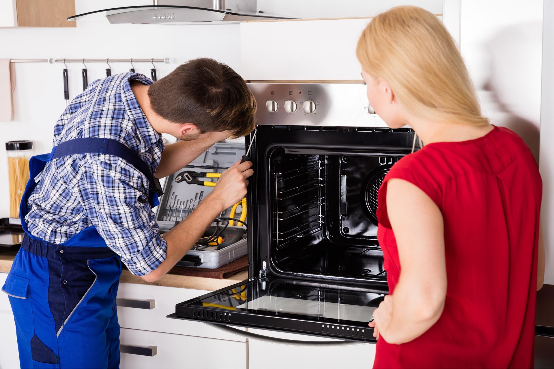 a man and a woman are fixing an oven in a kitchen .