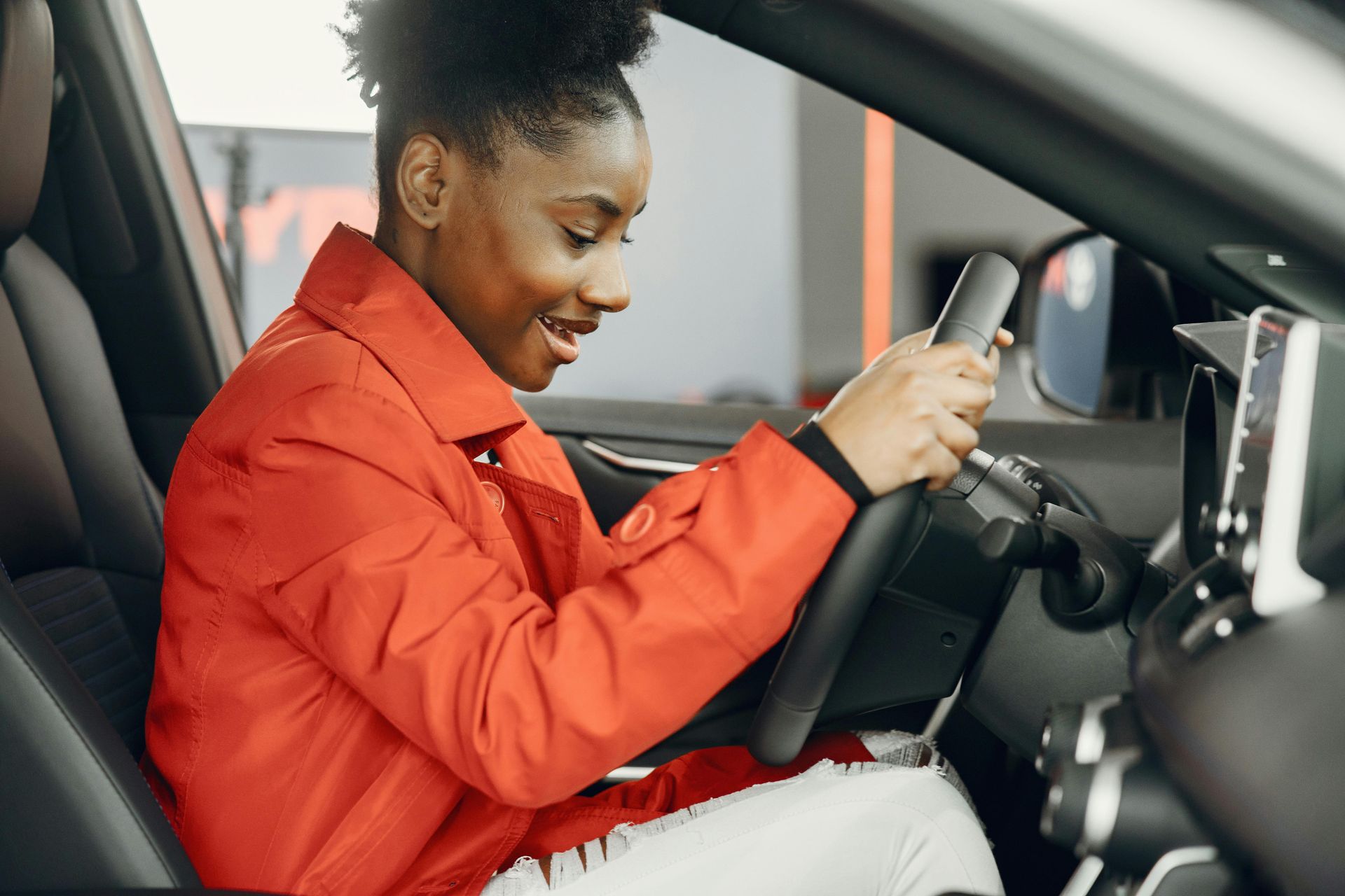 Woman sitting in driver's seat of a car, smiling, wearing a red jacket.