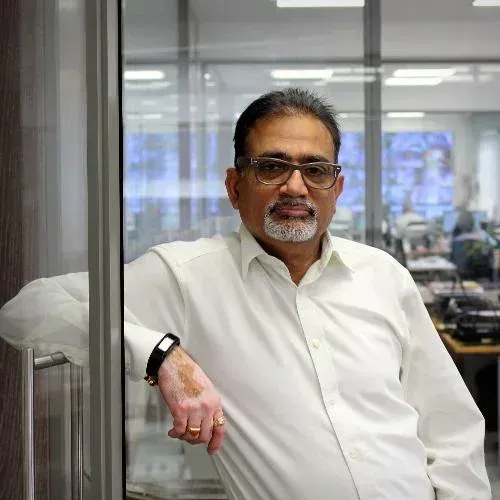 A man with a beard and glasses is leaning against a glass door. The mans name is Bharat.