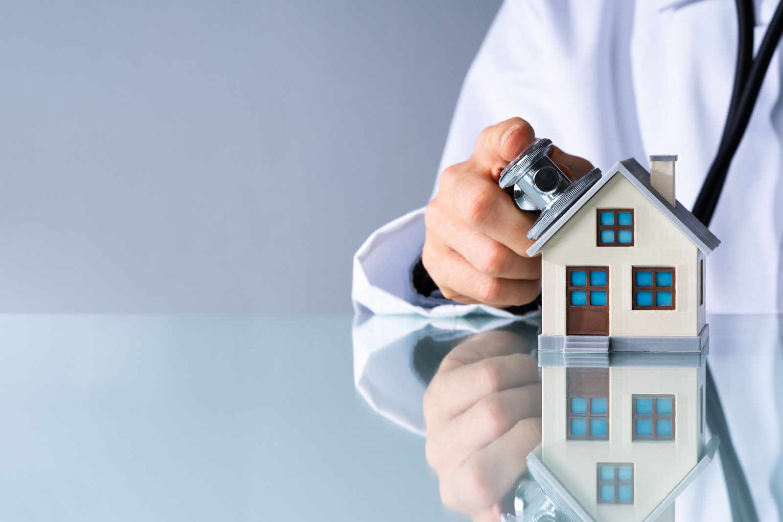 A doctor is holding a stethoscope over a model house.