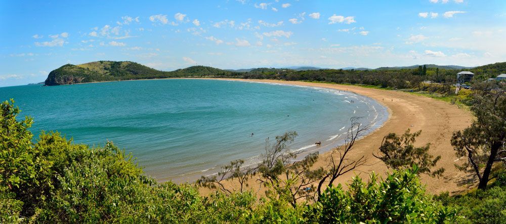 A Large Body Of Water With A Sandy Beach And Trees In The Foreground — Caves Coastal Physiotherapy in Doyalson, NSW