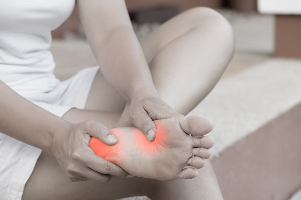 A Woman Is Sitting On A Bed Holding Her Foot In Pain — Caves Coastal Physiotherapy in Belmont, NSW