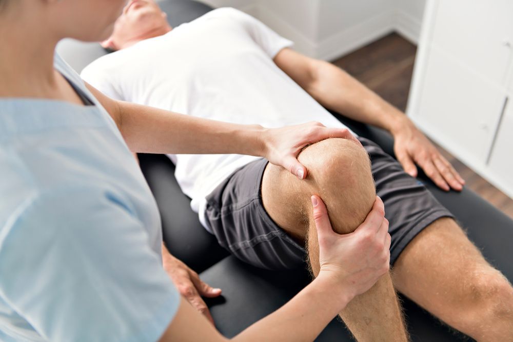 A Man Is Getting His Knee Examined By A Nurse — Caves Coastal Physiotherapy in Belmont, NSW
