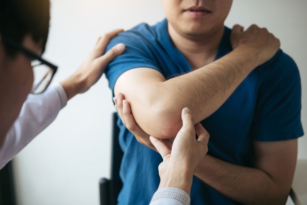 A Man Is Getting His Elbow Examined By A Doctor — Caves Coastal Physiotherapy in Belmont, NSW