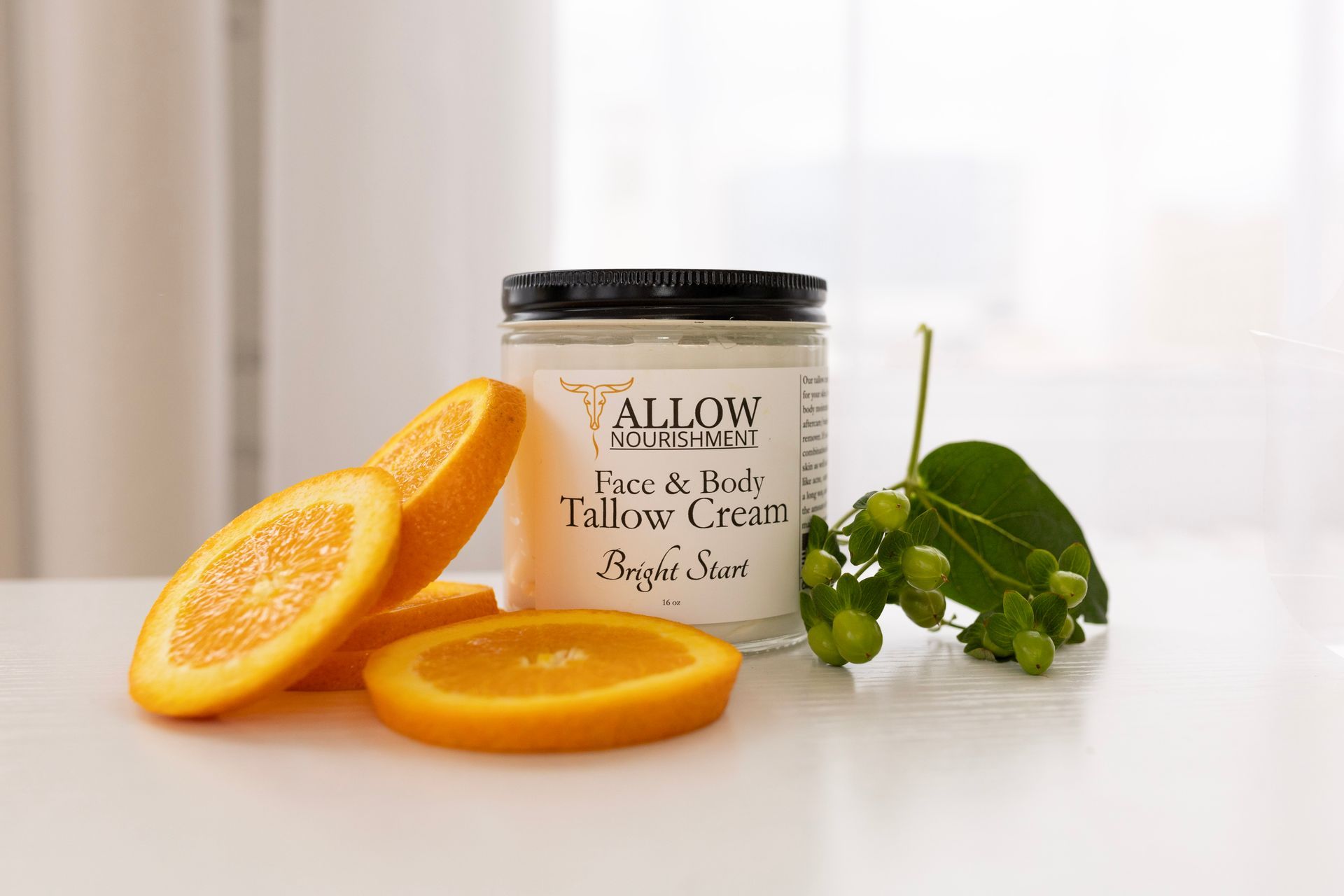 a jar of Allow Nourishments tallow cream is sitting on a table next to sliced oranges .