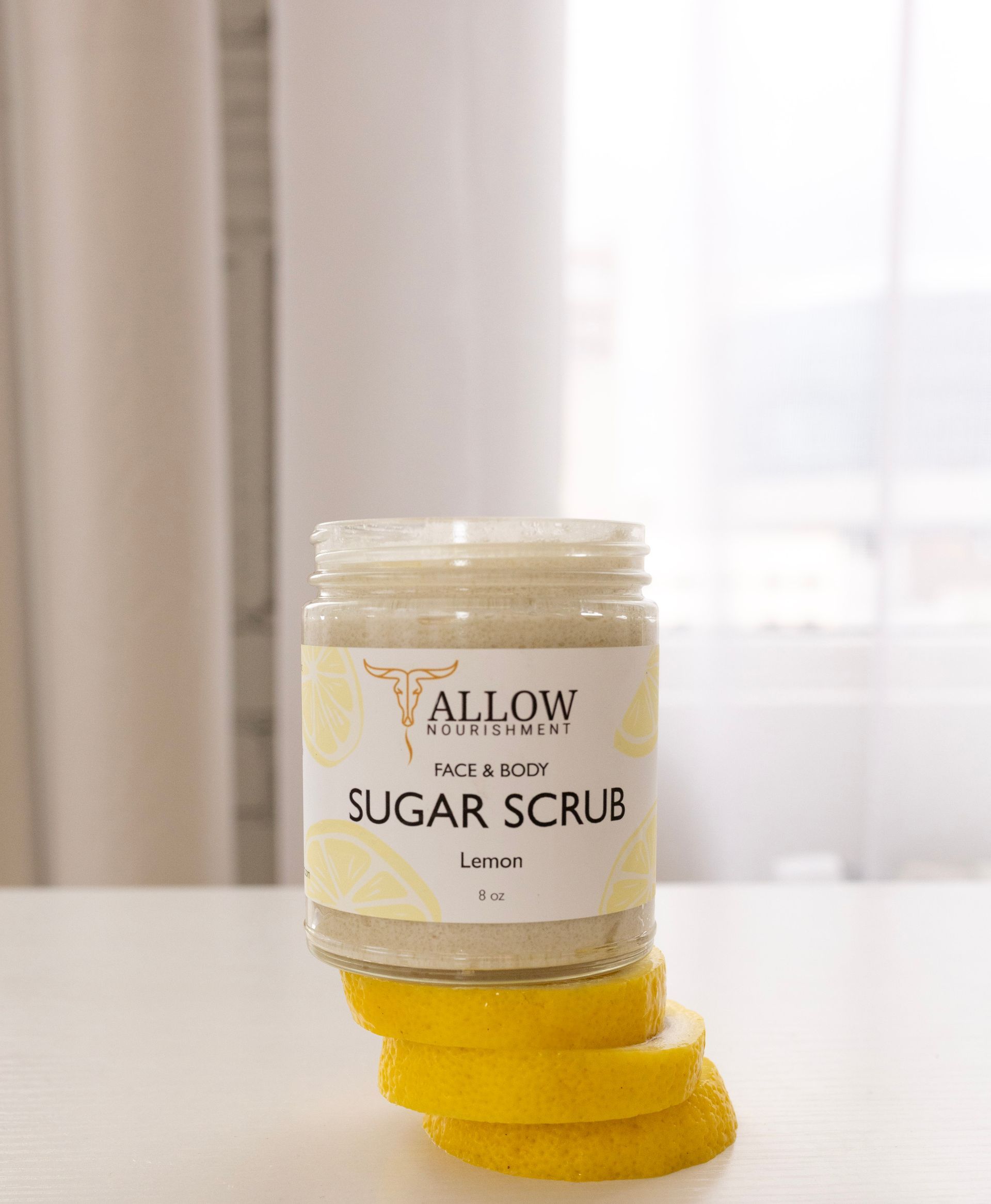 A jar of sugar scrub is sitting on a table next to lemon slices.