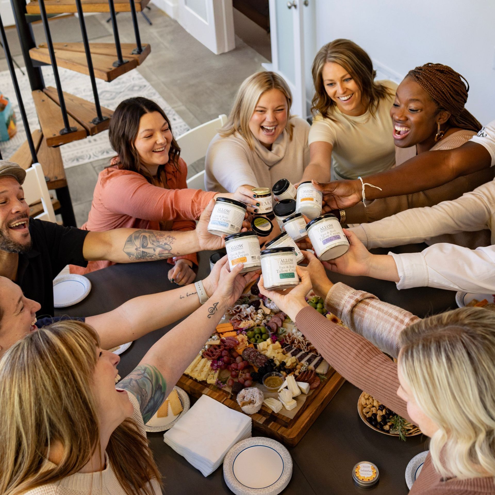 A group of people are sitting around a table toasting with jars of tallow.