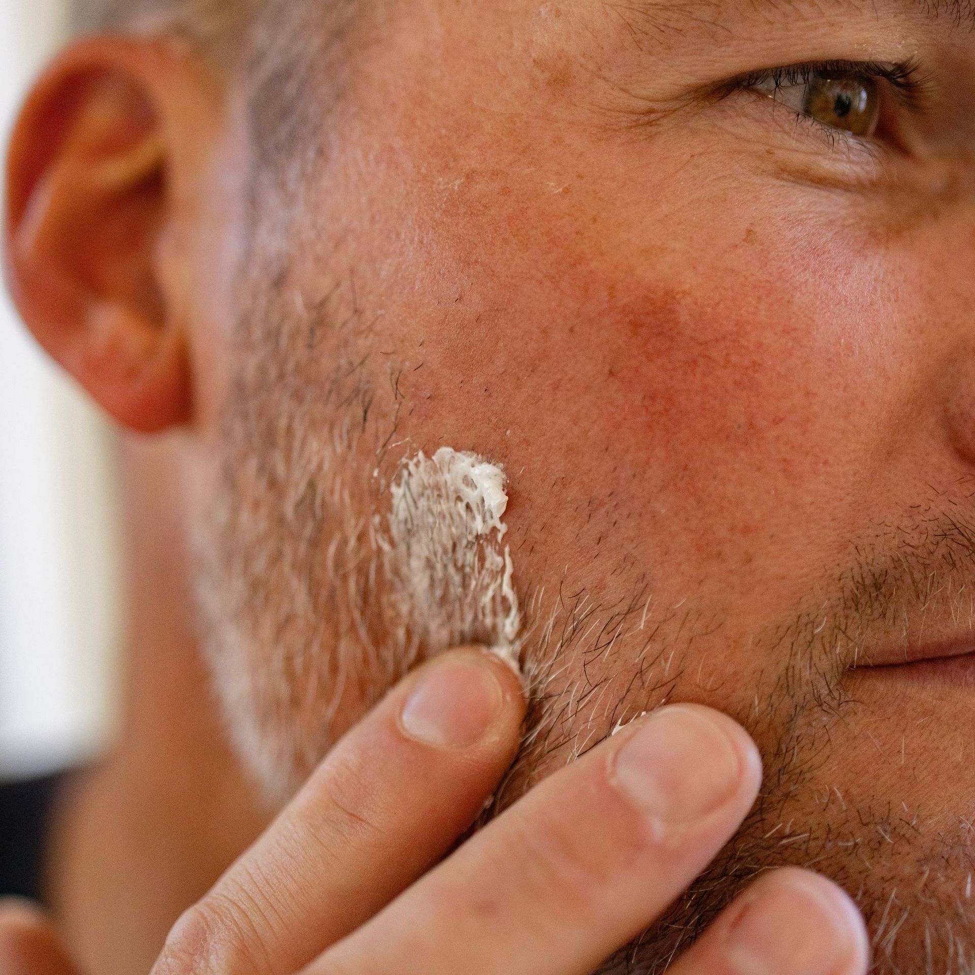 A man with a beard is applying tallow cream to his face