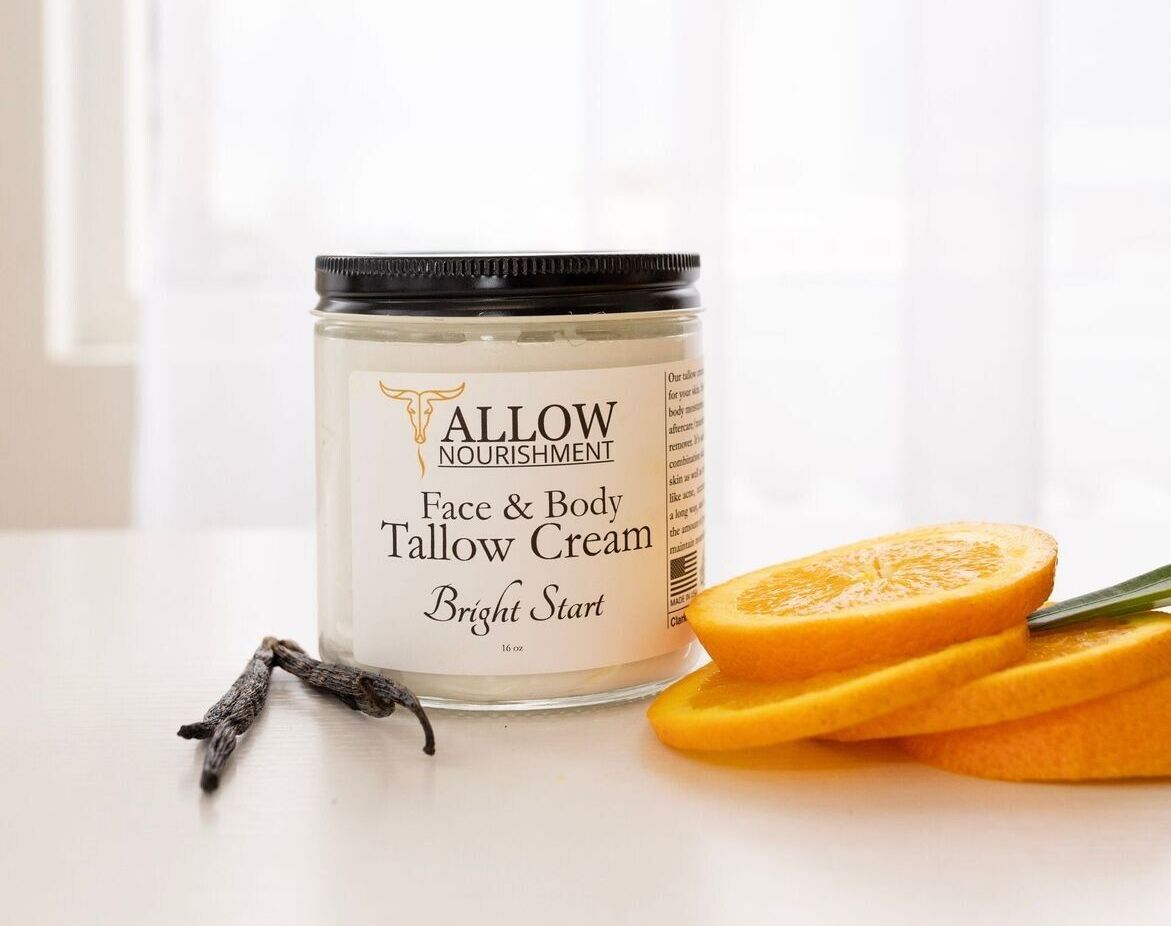 a jar of tallow cream is sitting on a table next to sliced oranges .