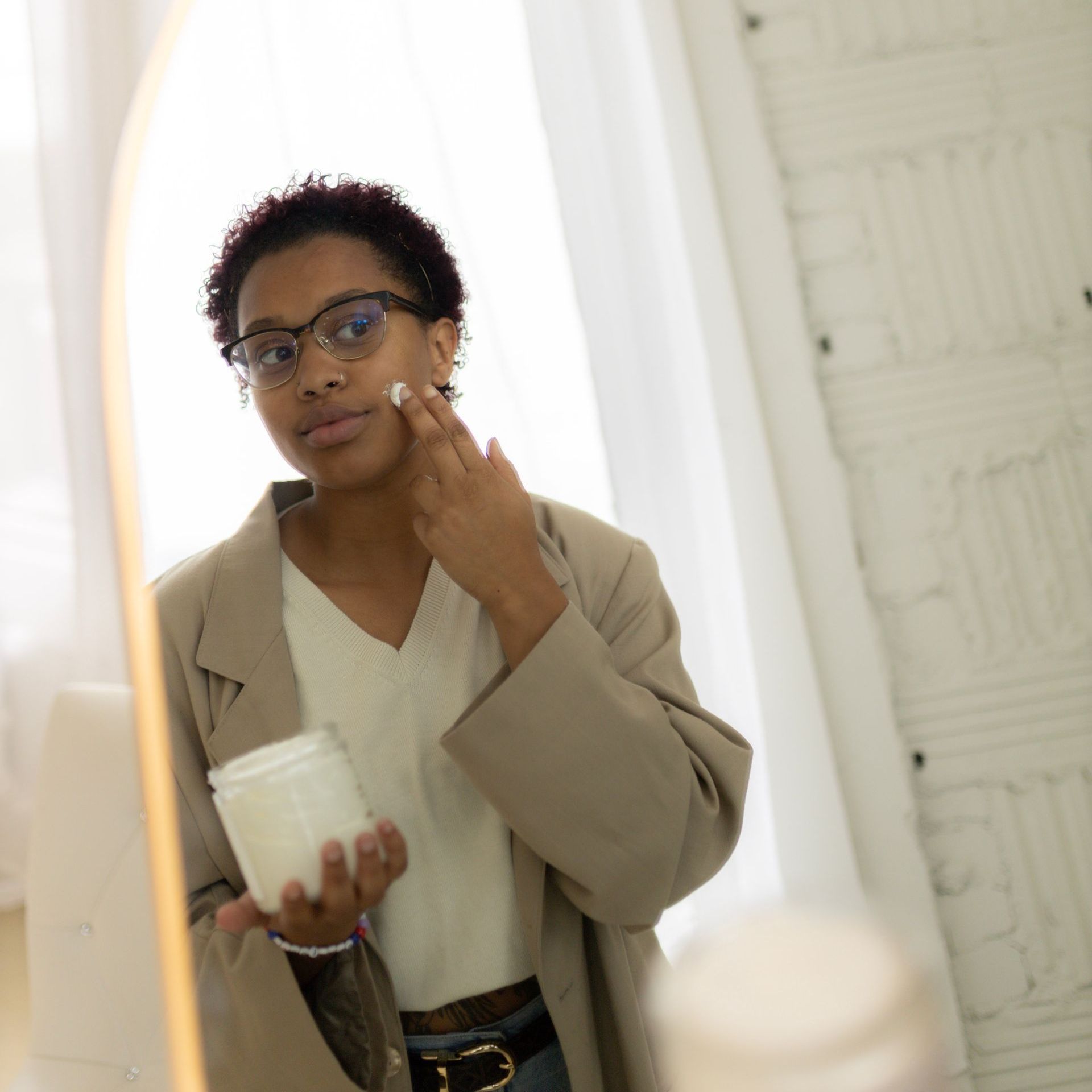 A woman putting Allow Nourishment Tallow Face & Body Cream on her face. 