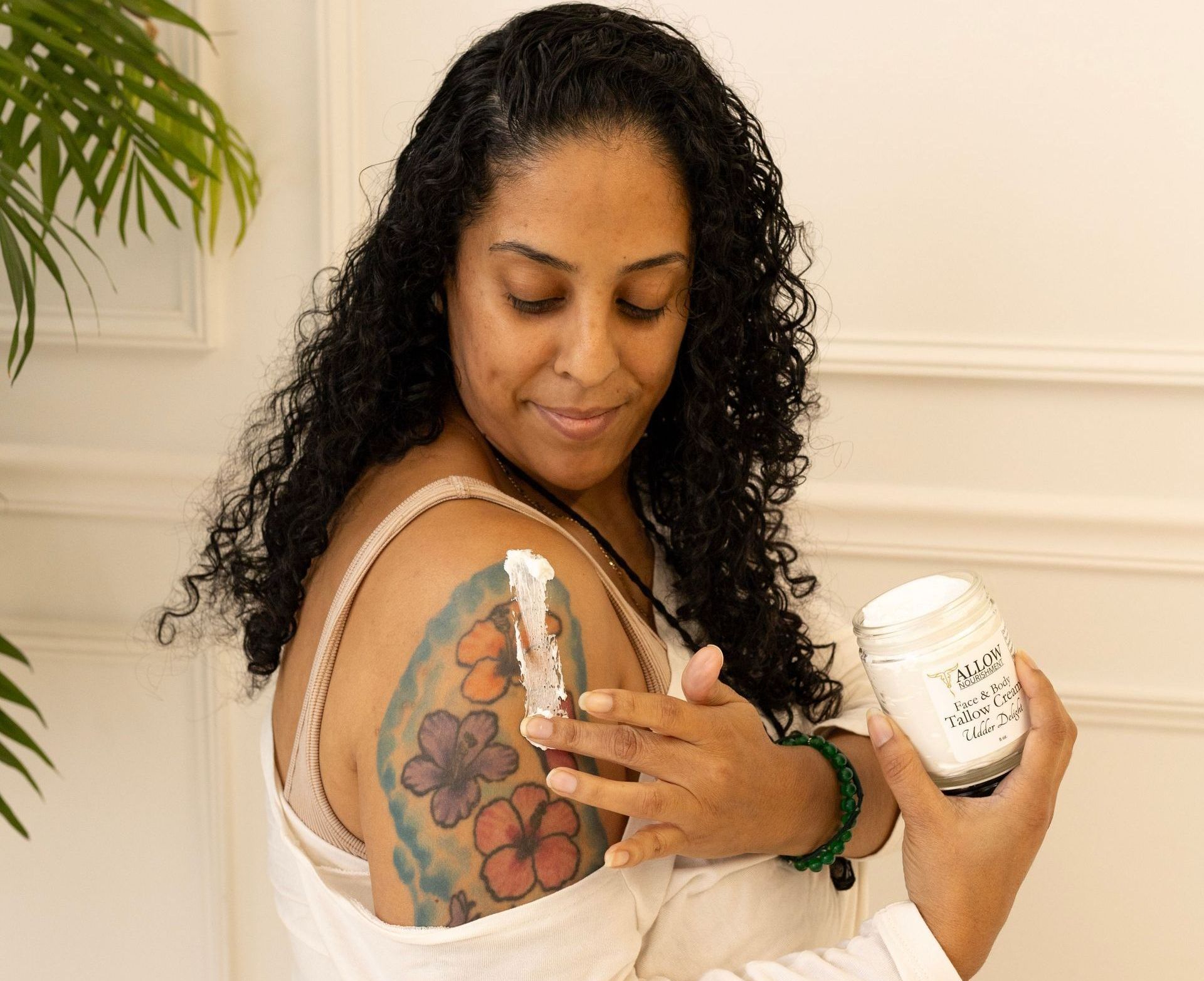 A woman applying Allow Nourishment Tallow Face & Body Cream to a tattoo on her shoulder. 