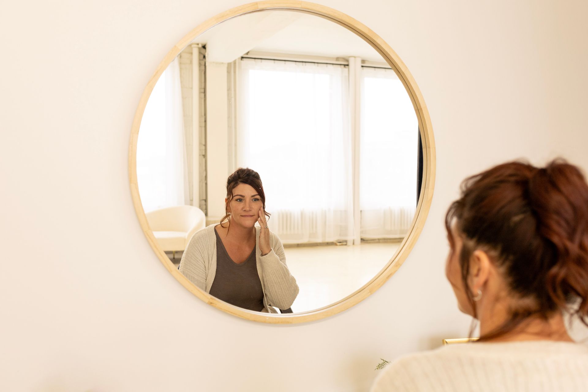 A woman looking in the mirror while putting tallow face and body cream on her face