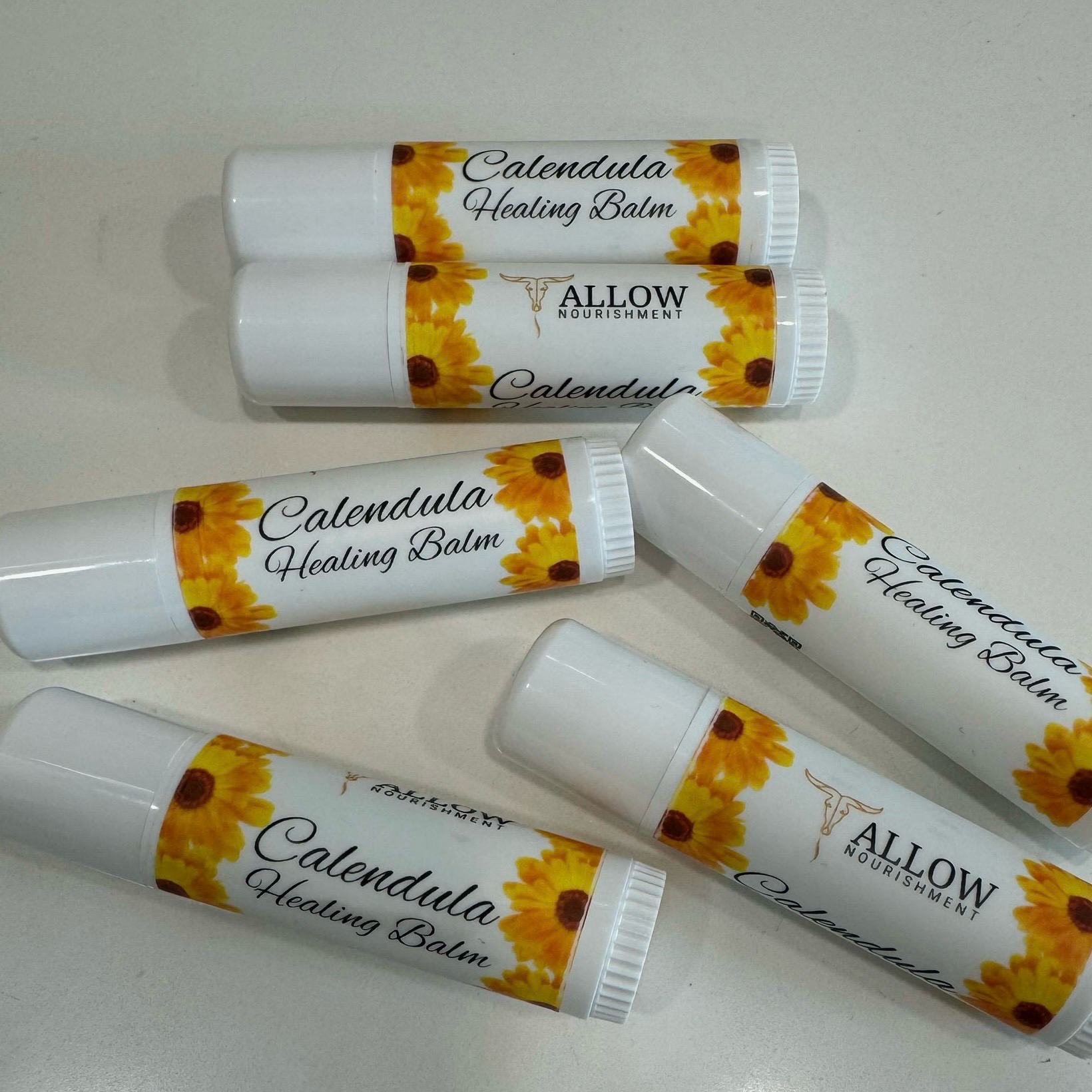 Allow Nourishment / Several tubes of calendula healing balm are sitting on a table.