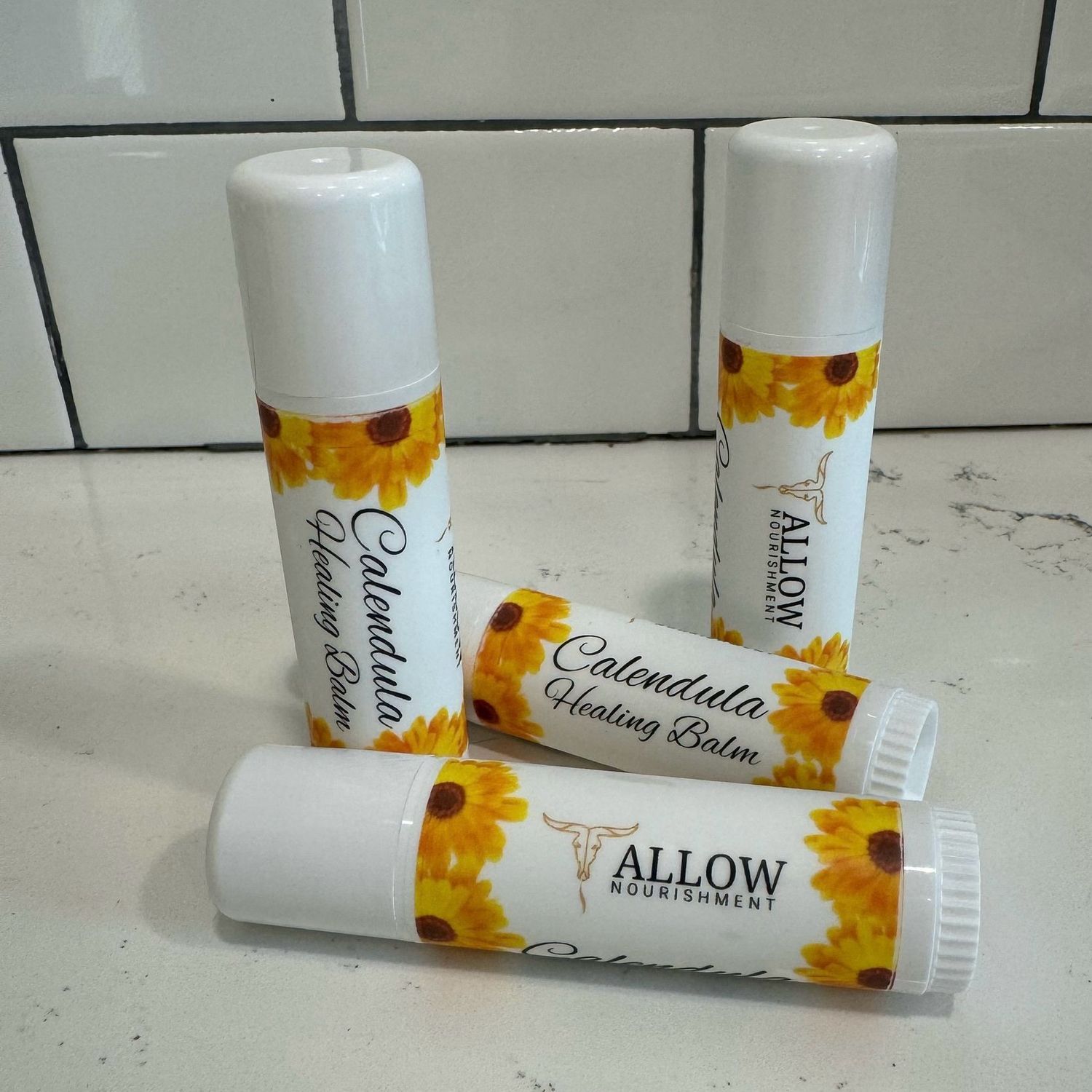 Allow Nourishment / Four tubes of calendula moisturizing balm are sitting on a counter.