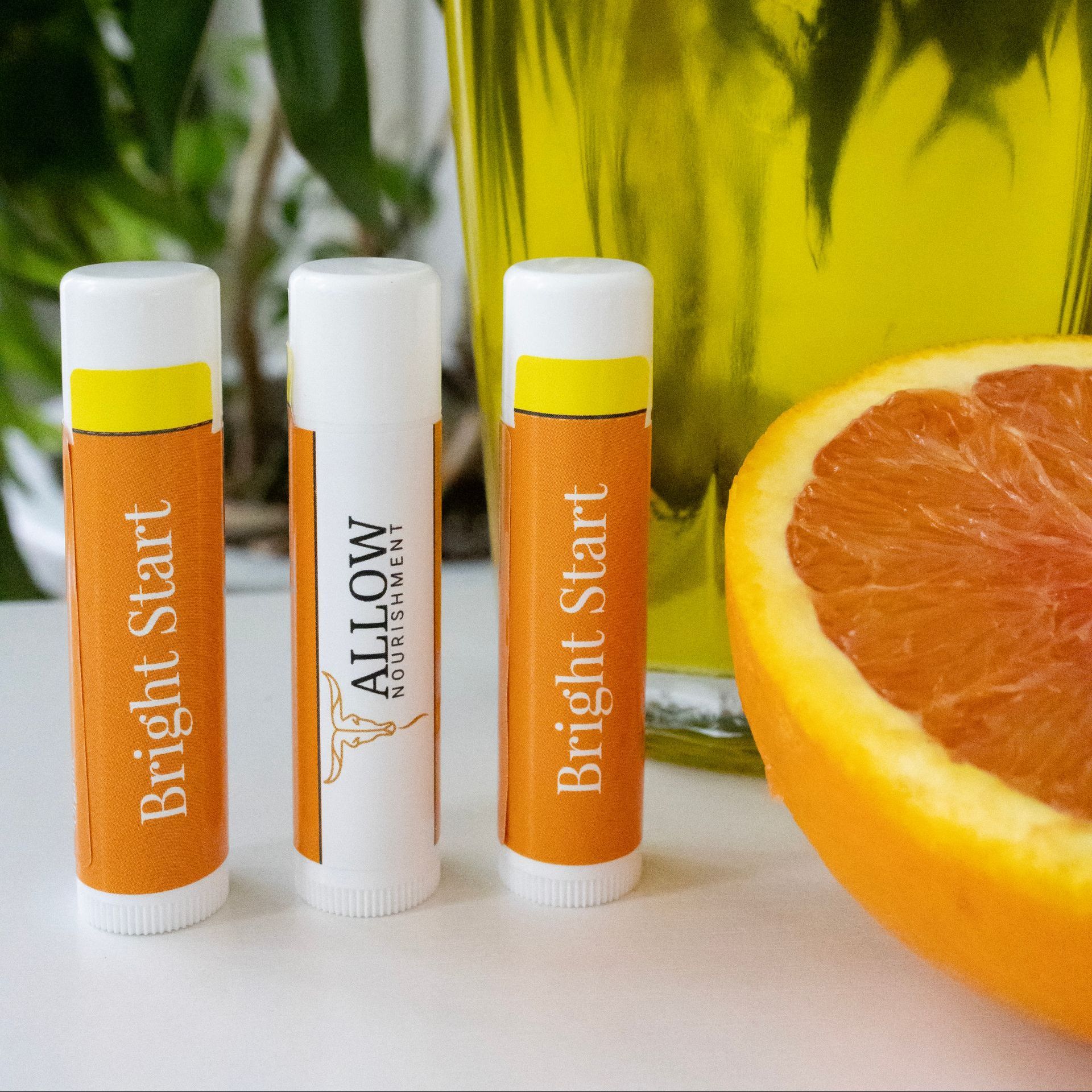 Three tubes of bright start lip balm next to an orange.