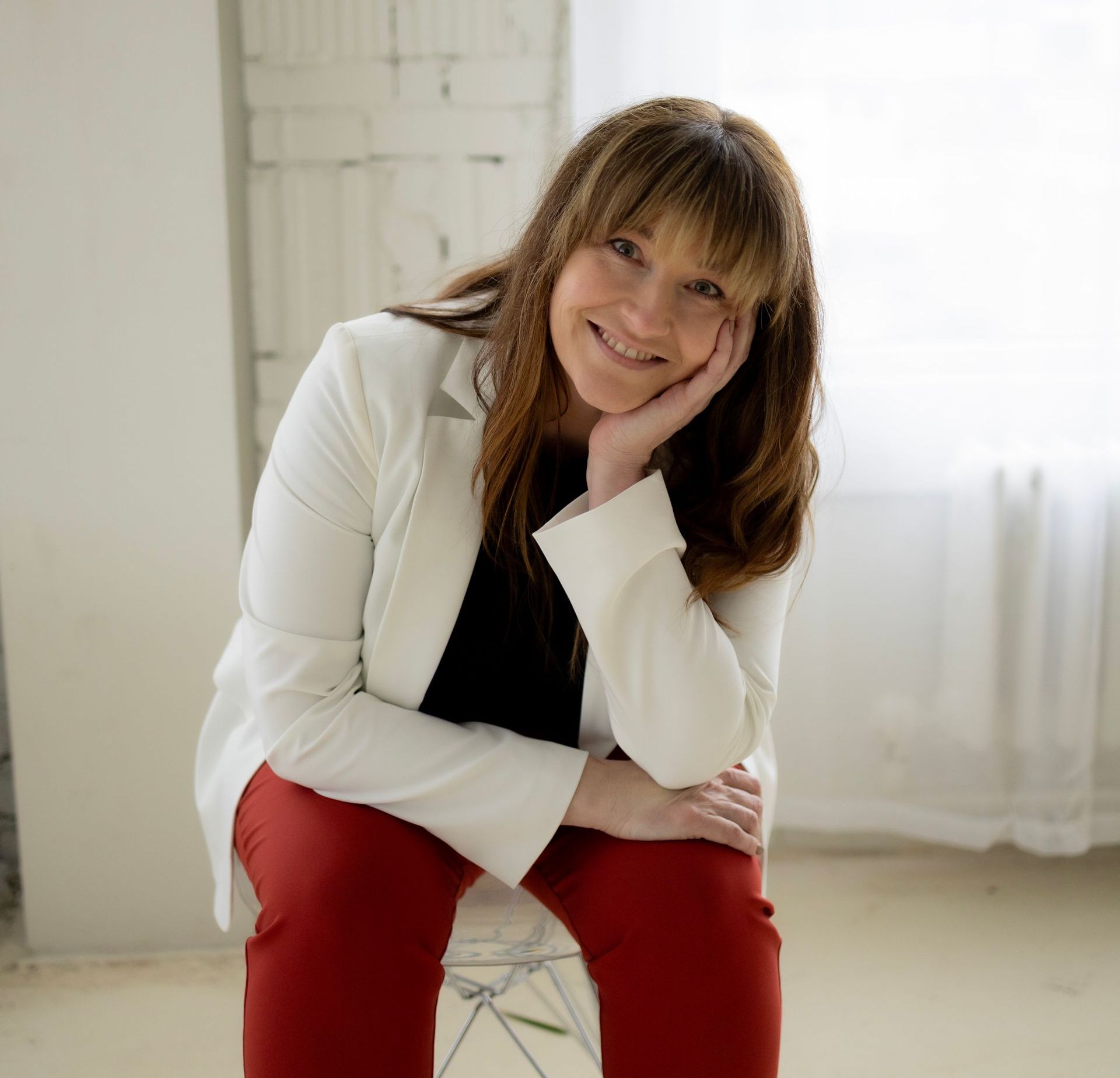 Brie Bacon, Founder of Allow Nourishment in a white jacket and red pants is sitting on a chair