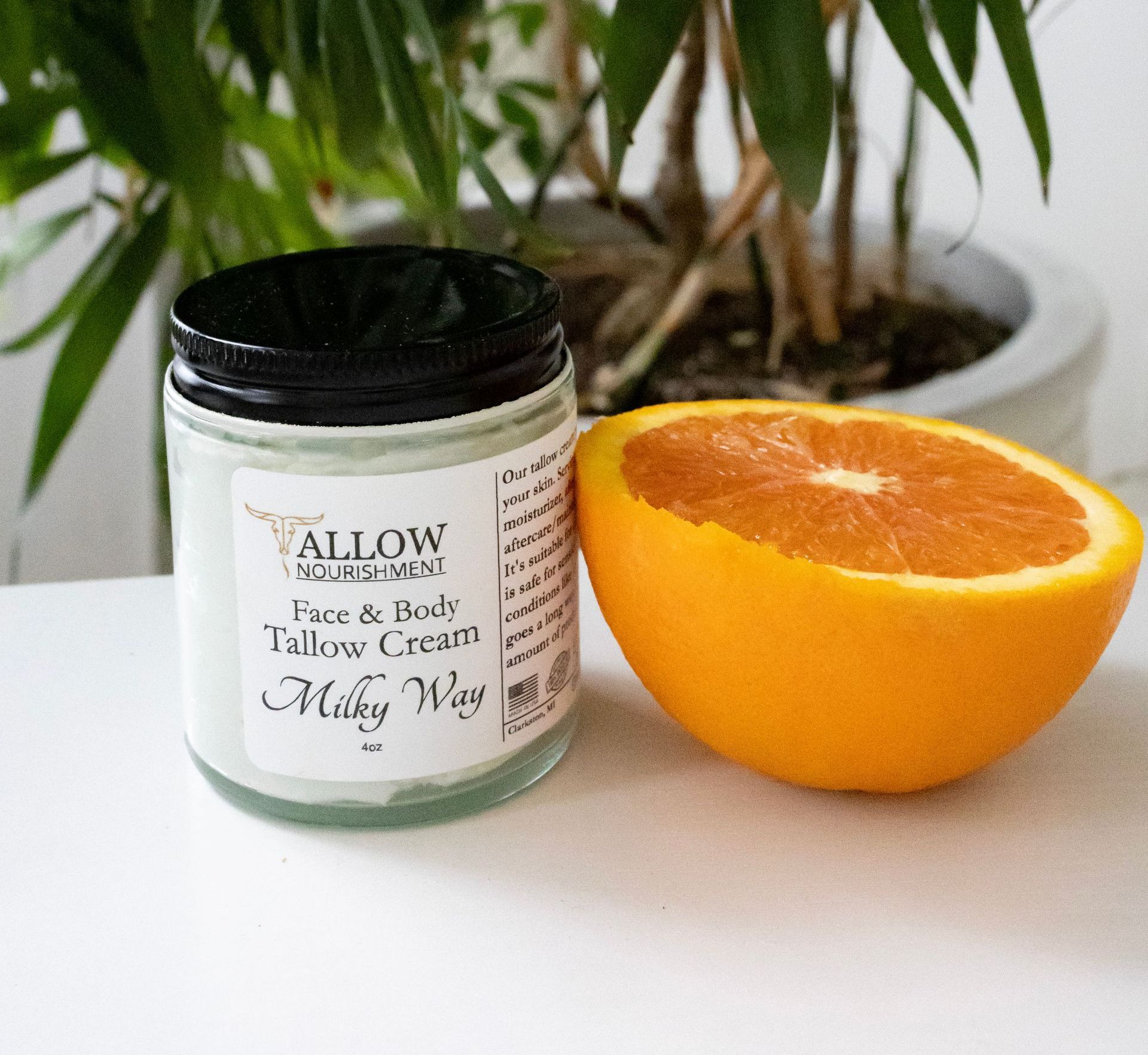 A jar of Allow Nourishment milky way tallow face & body cream next to a sliced orange