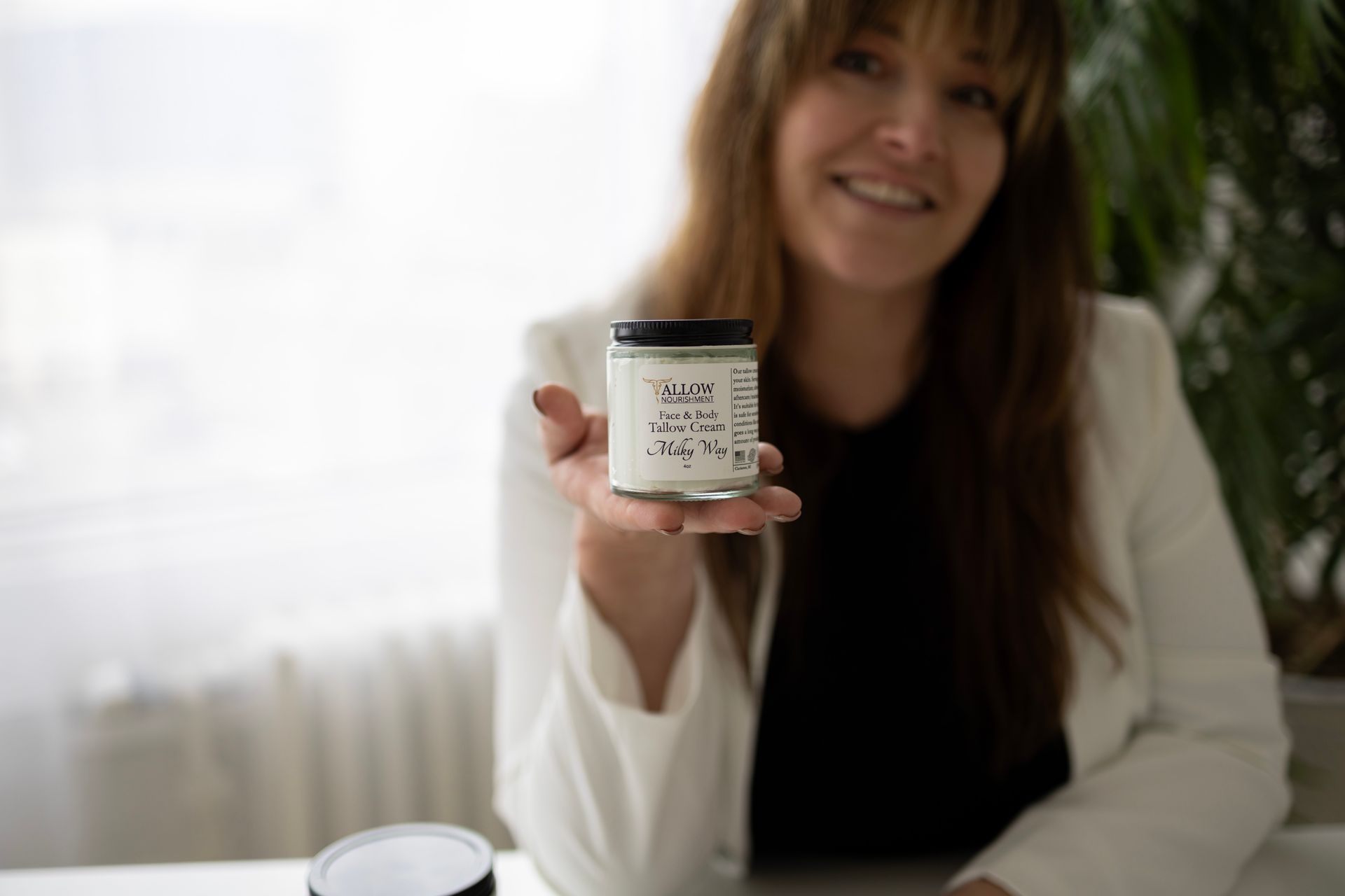 a woman is holding a jar of tallow cream in her hand.