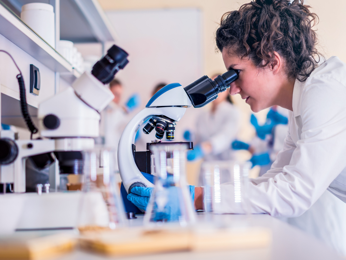 A woman is looking through a microscope in a laboratory.