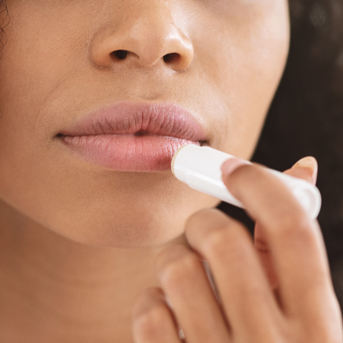 A woman is applying Allow Nourishment lip balm to her lips.