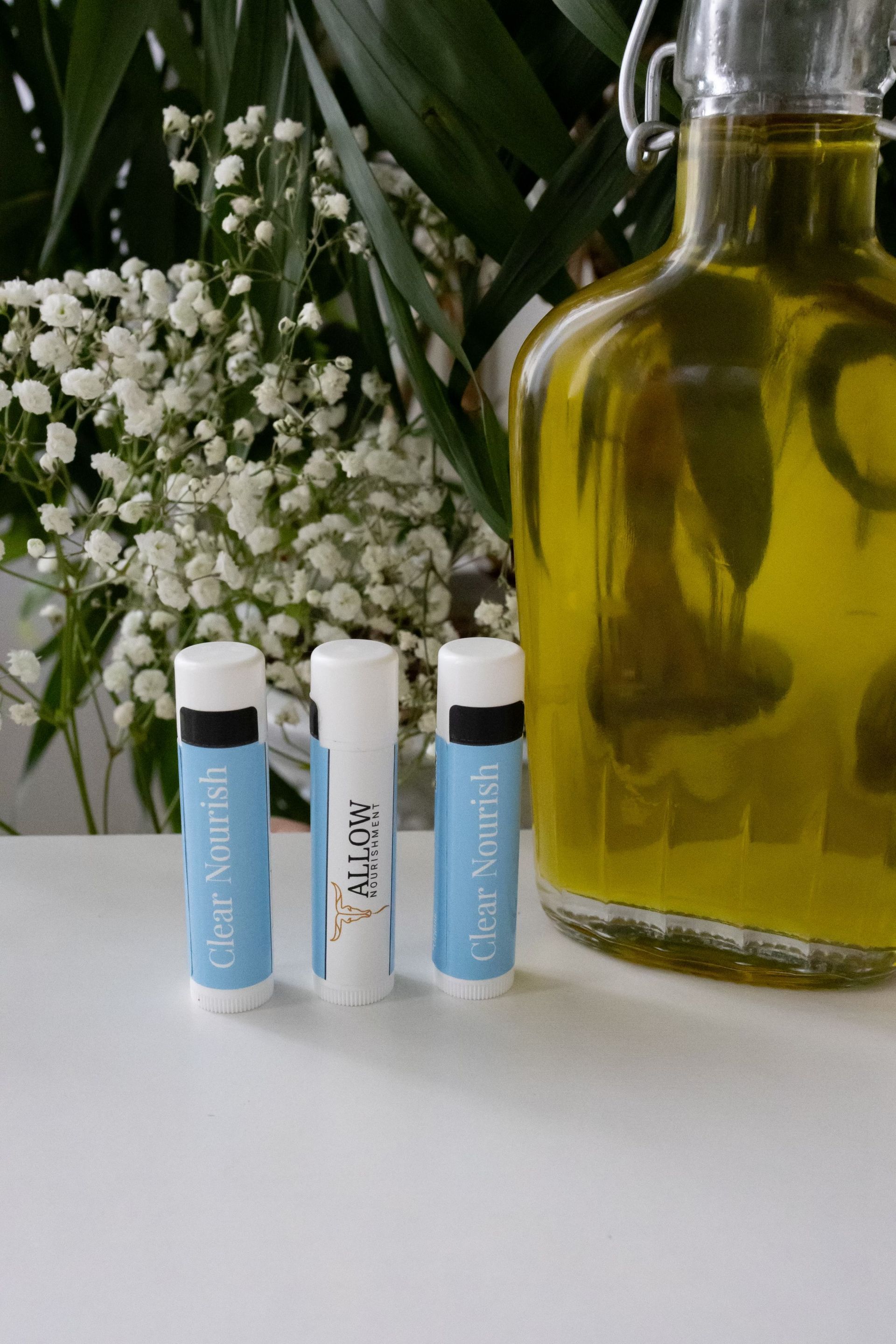 Three Allow Nourishment Tallow lip balms are sitting on a table next to a bottle of olive oil.