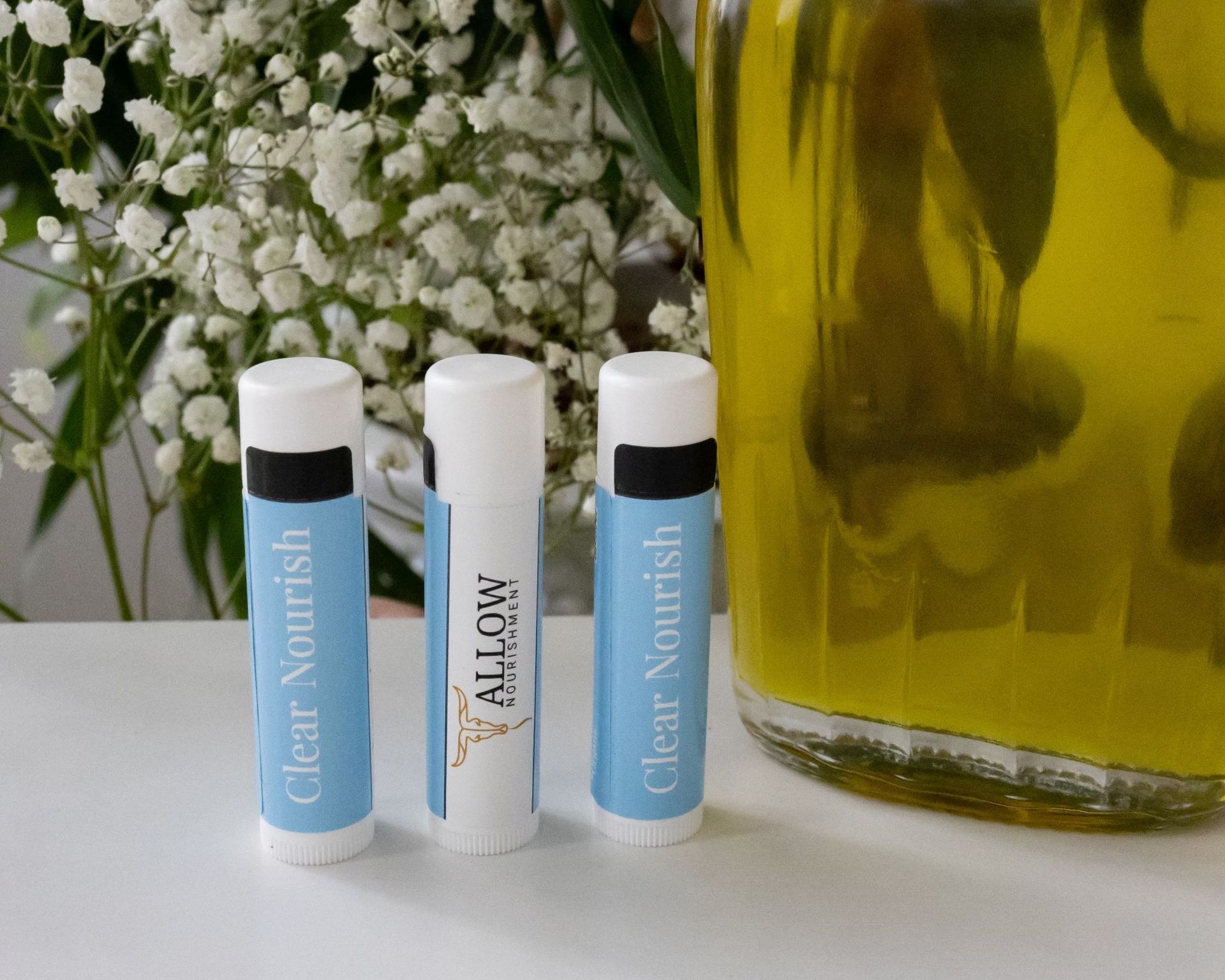 Three Allow Nourishment Clear Nourish lip balms beside olive oil