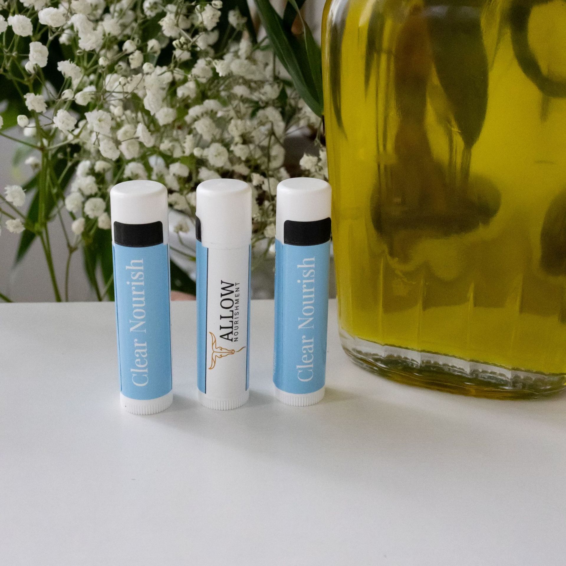 Three tubes of Allow Nourishment clear nourish lip balm on a table