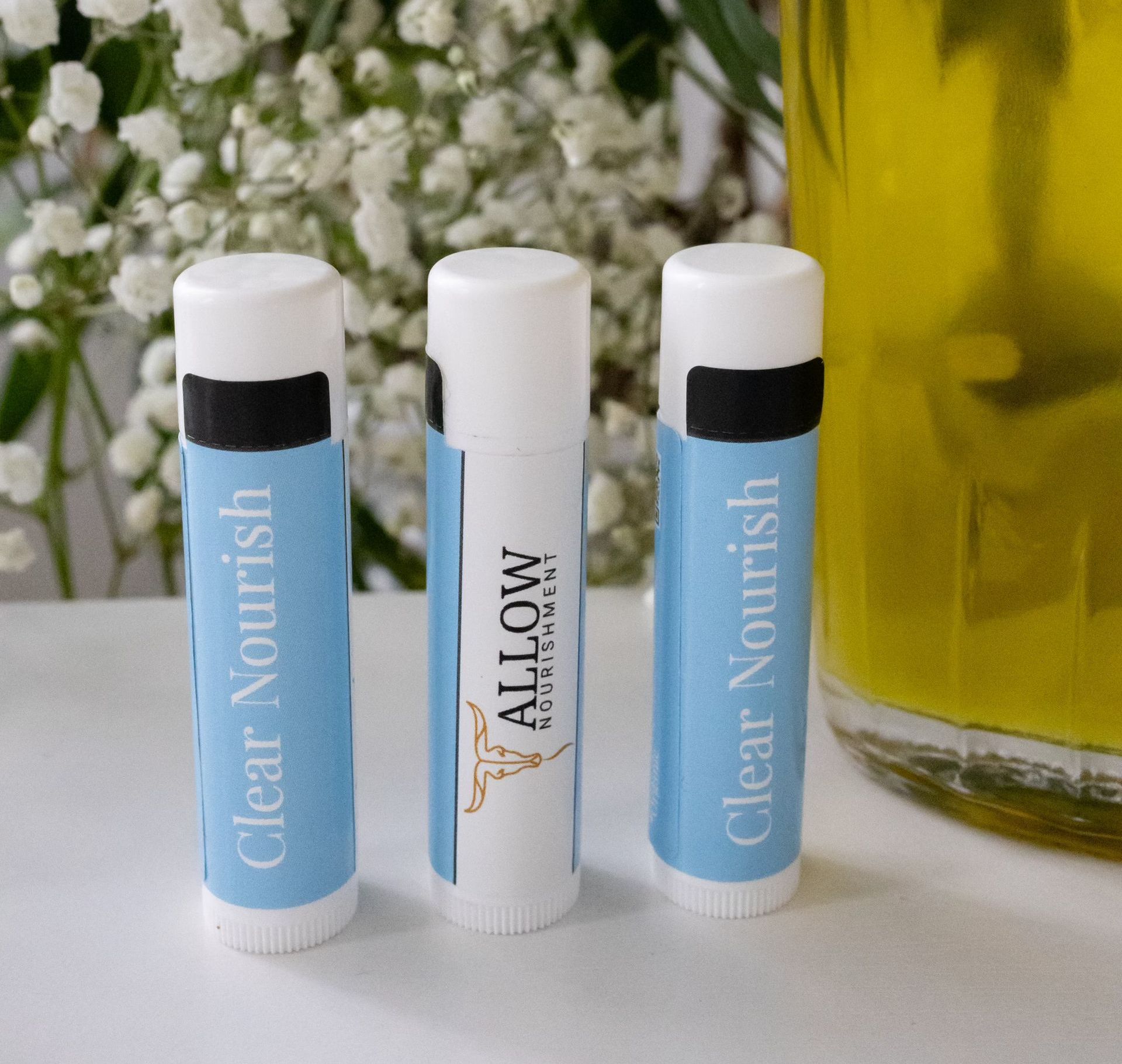 three lip balms are sitting on a table next to a bottle of oil .