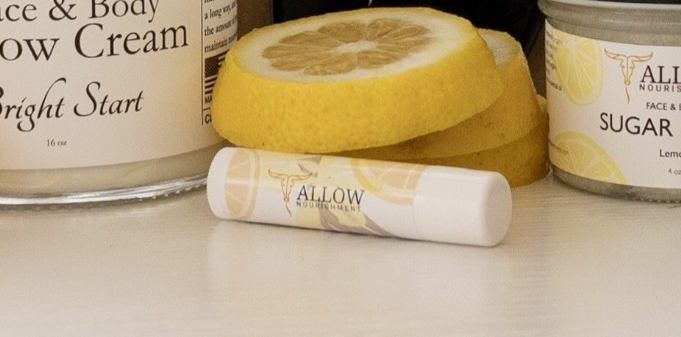 a lip balm is sitting on a table next to a jar of cream and lemon slices .