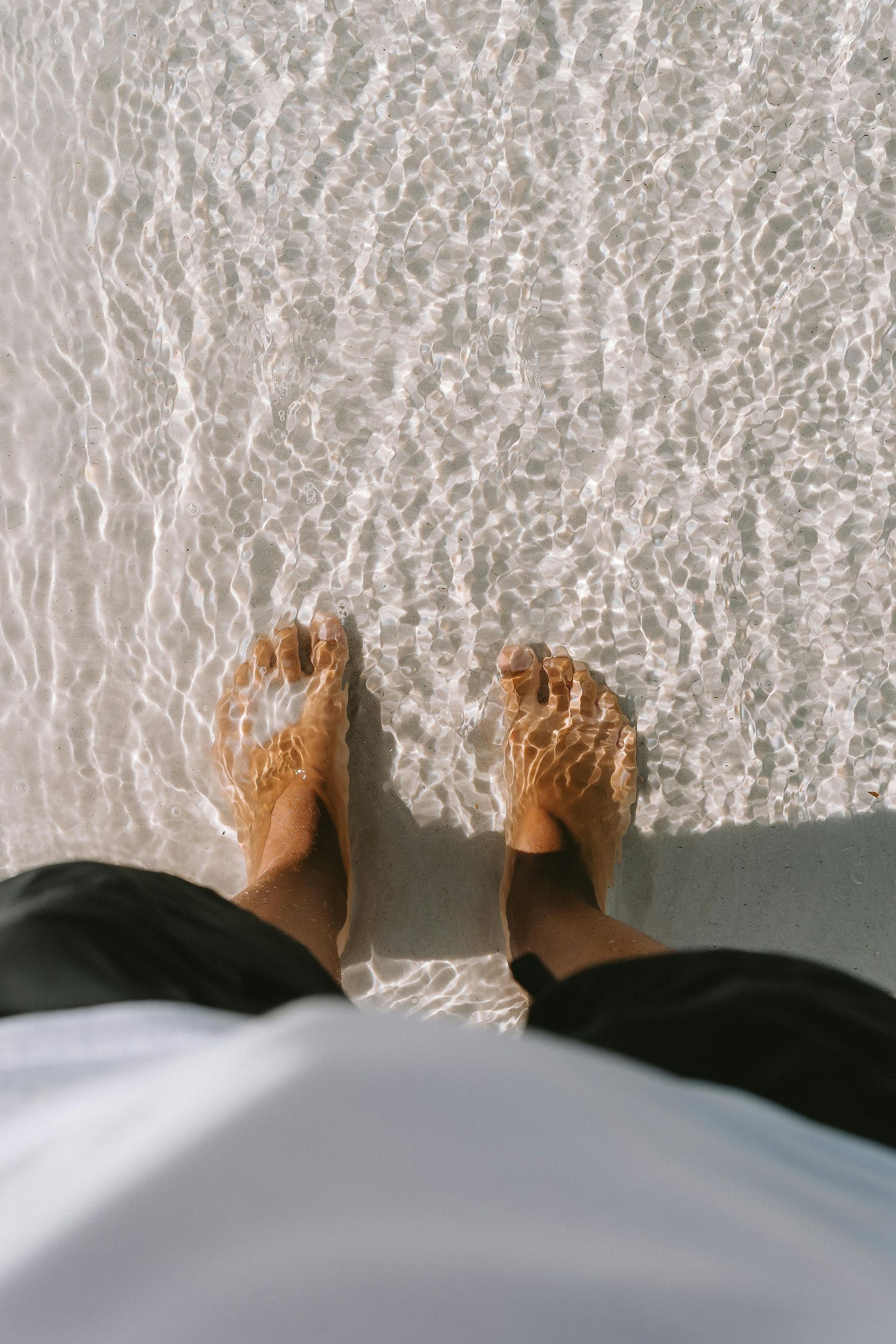 A person 's feet are standing in the sand on a beach.