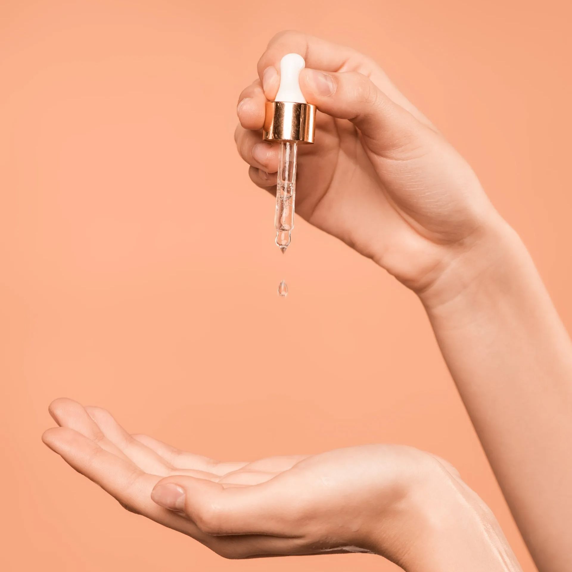 A woman is holding a pipette with a drop of emu oil coming out of it.