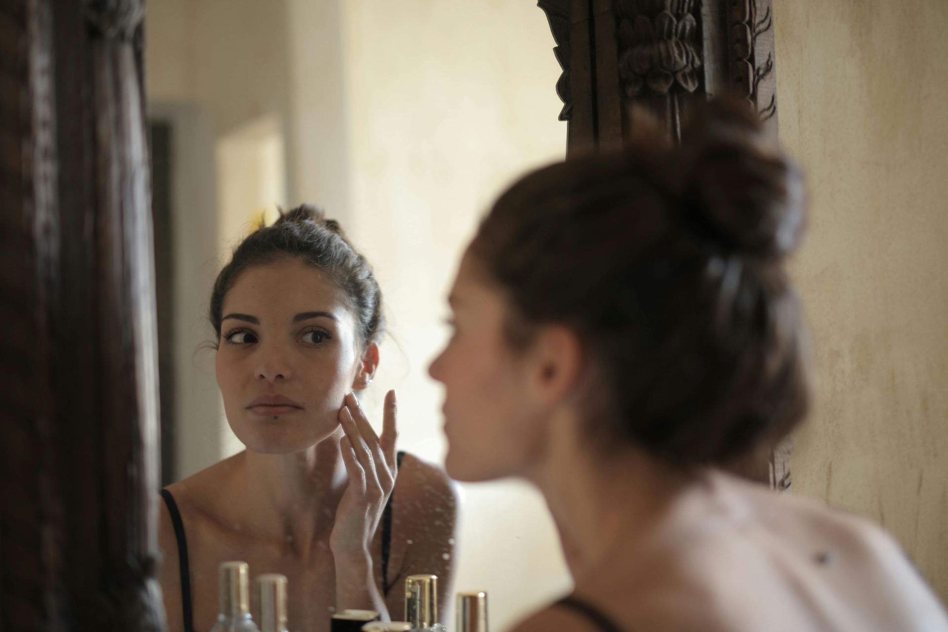 A woman is looking at her face in a mirror.