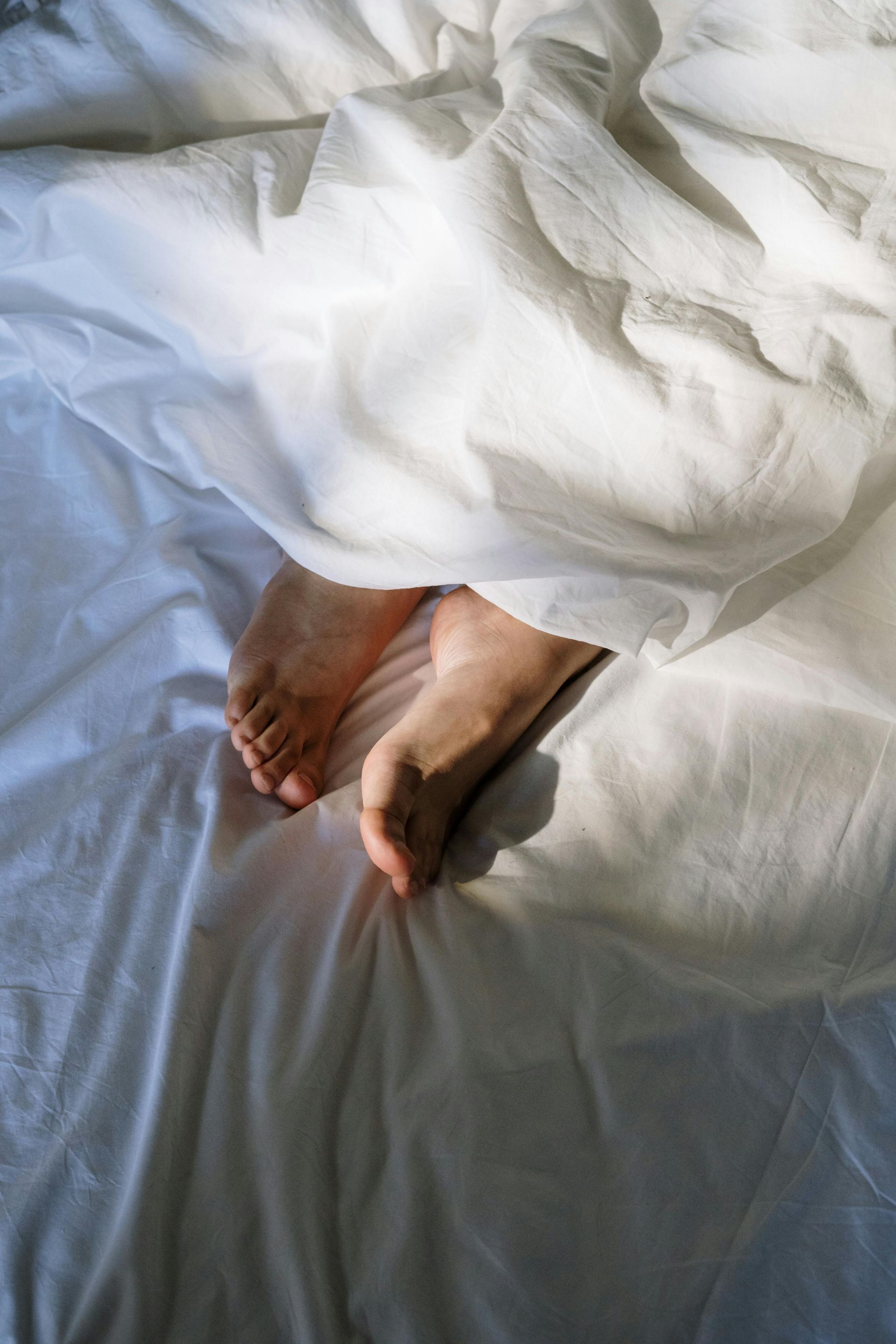 A person 's feet are sticking out of the blankets on a bed.