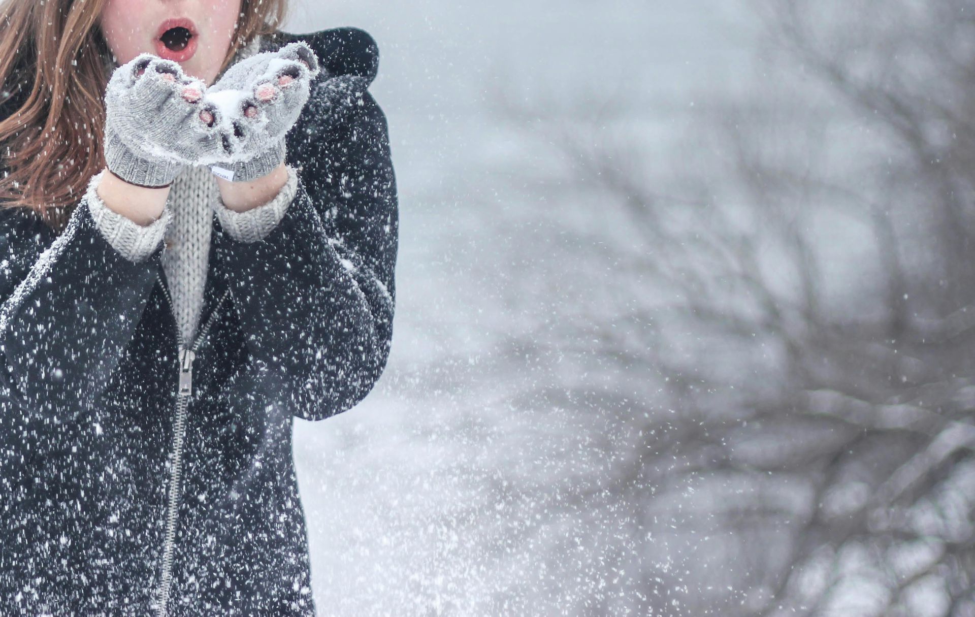 A woman is blowing snow from her hands in the winter.