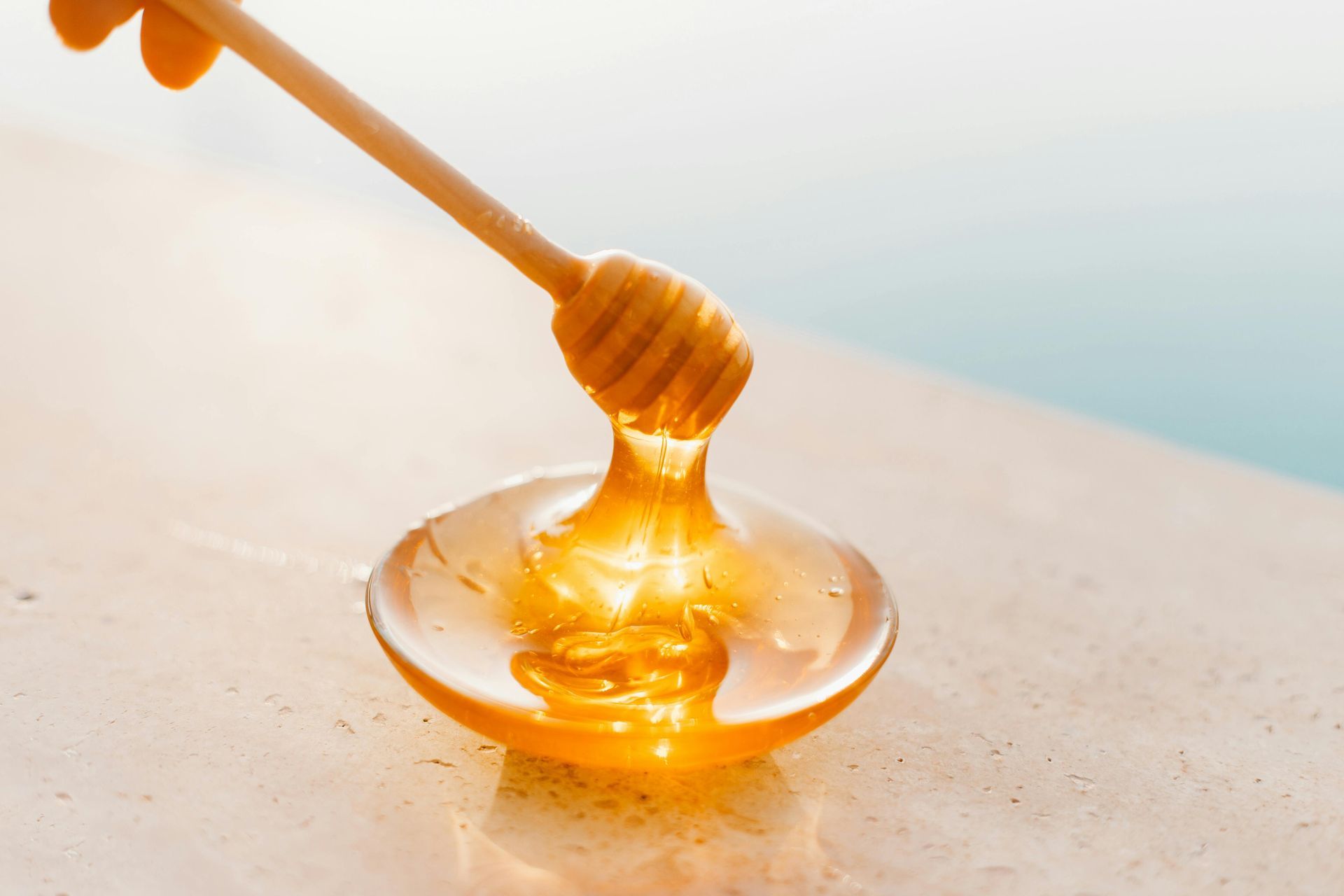 A person is pouring honey from a honey dipper into a bowl.