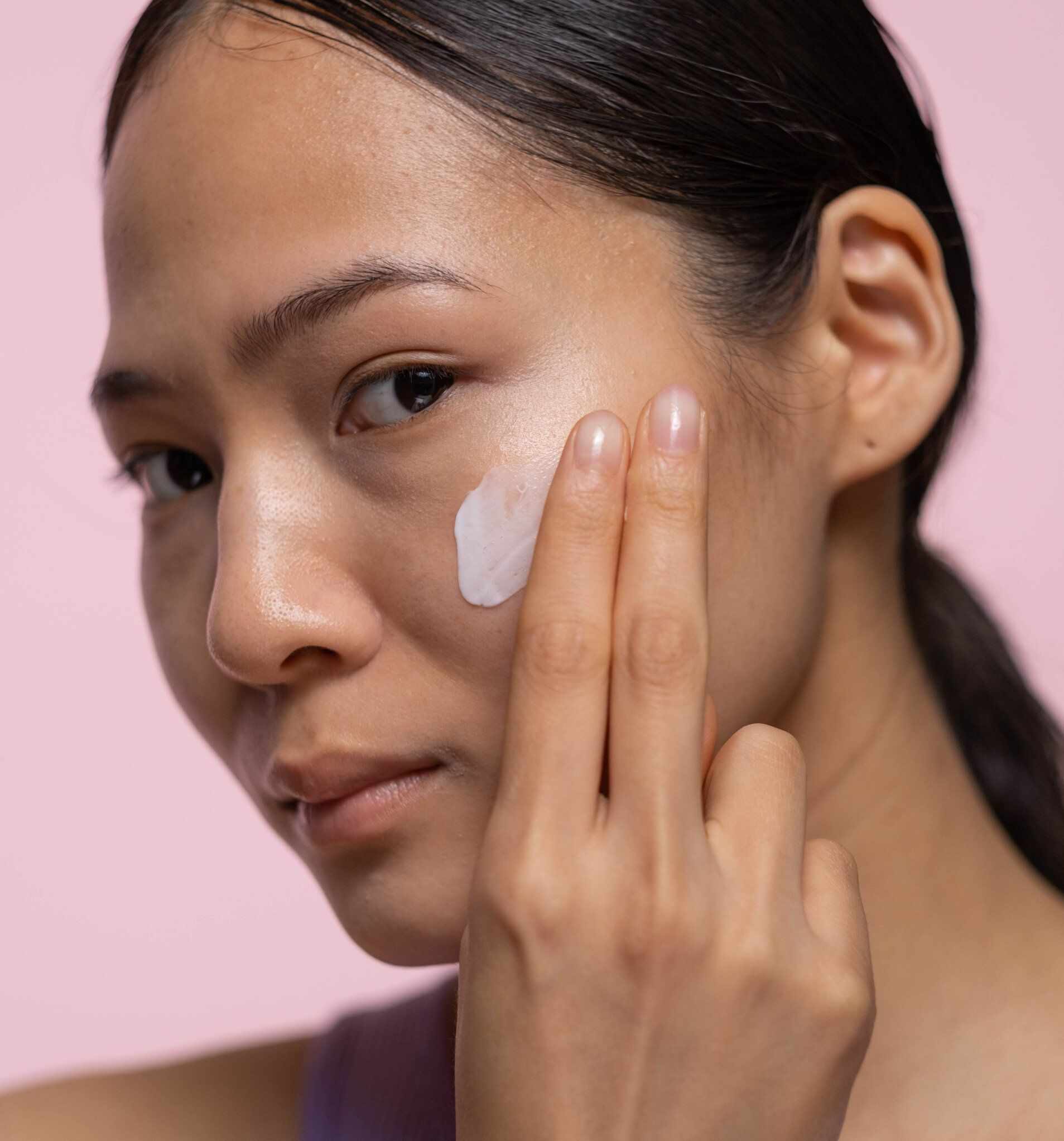 a woman is applying a cream to her face.