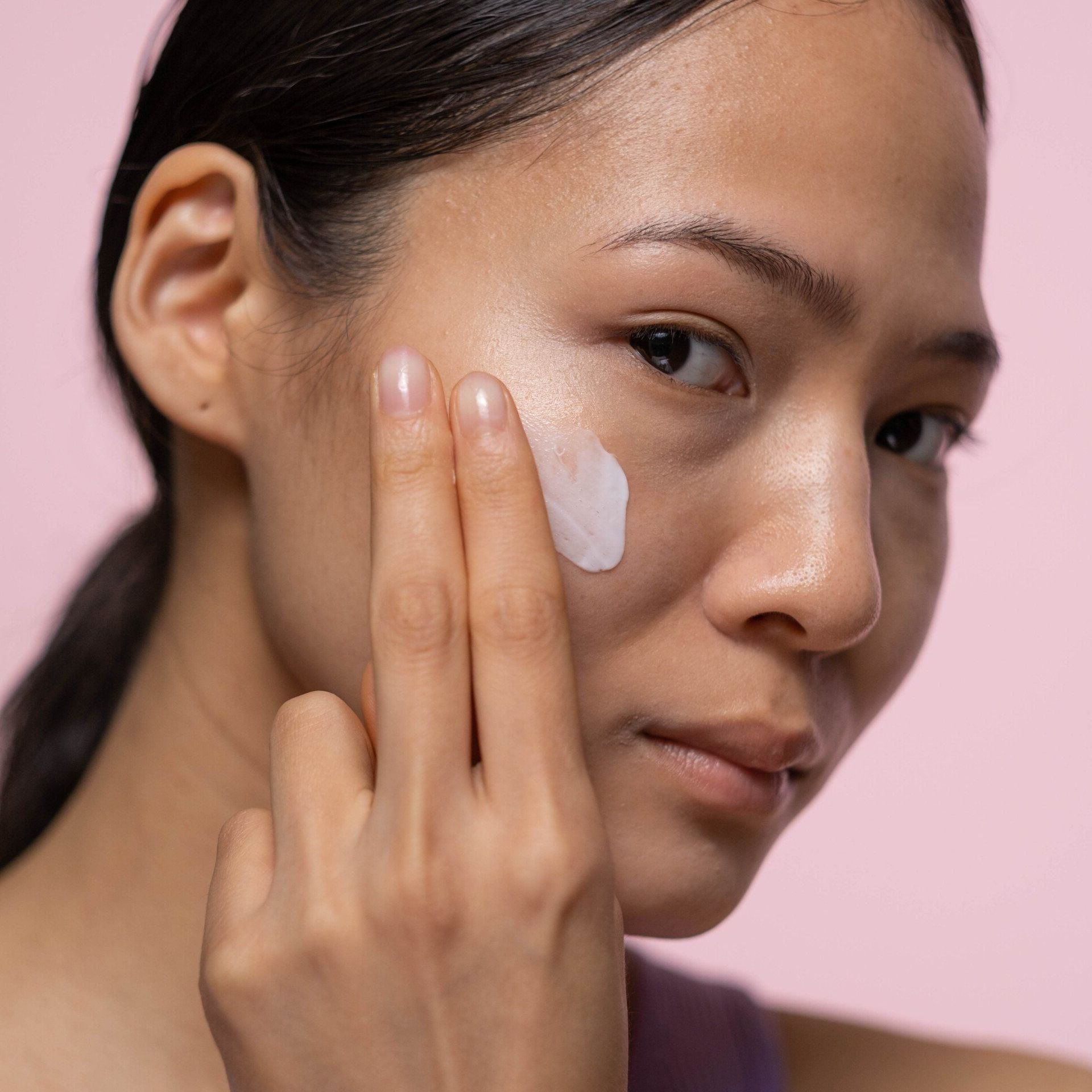 A young woman putting Allow Nourishment Tallow Face & Body Cream on her face.