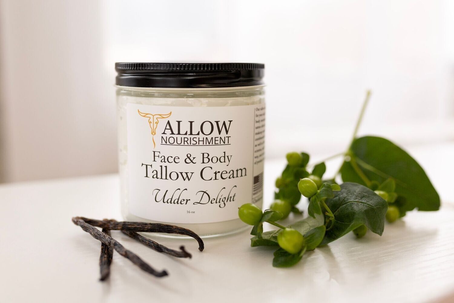 A jar of tallow cream is sitting on a table next to vanilla beans.