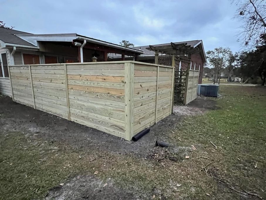 Wooden privacy fence outside a house, light brown boards. Cloudy sky, green grass, and a glimpse of a pergola.