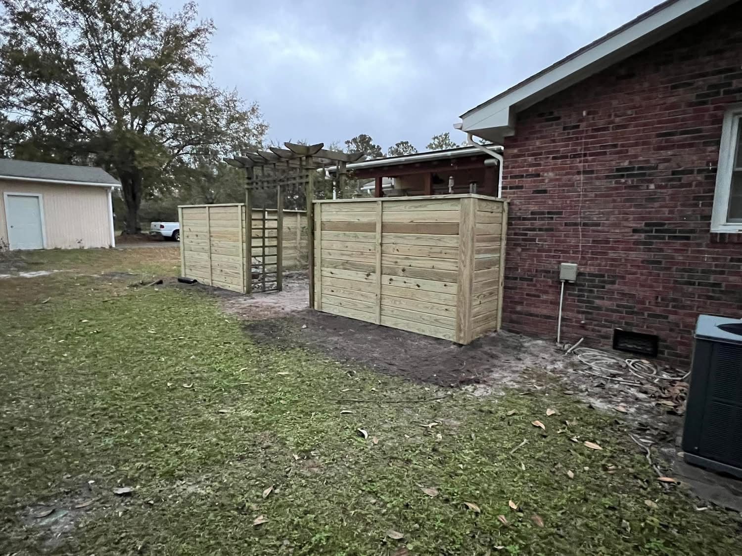 Wooden privacy fence with a pergola in a backyard next to a brick house.