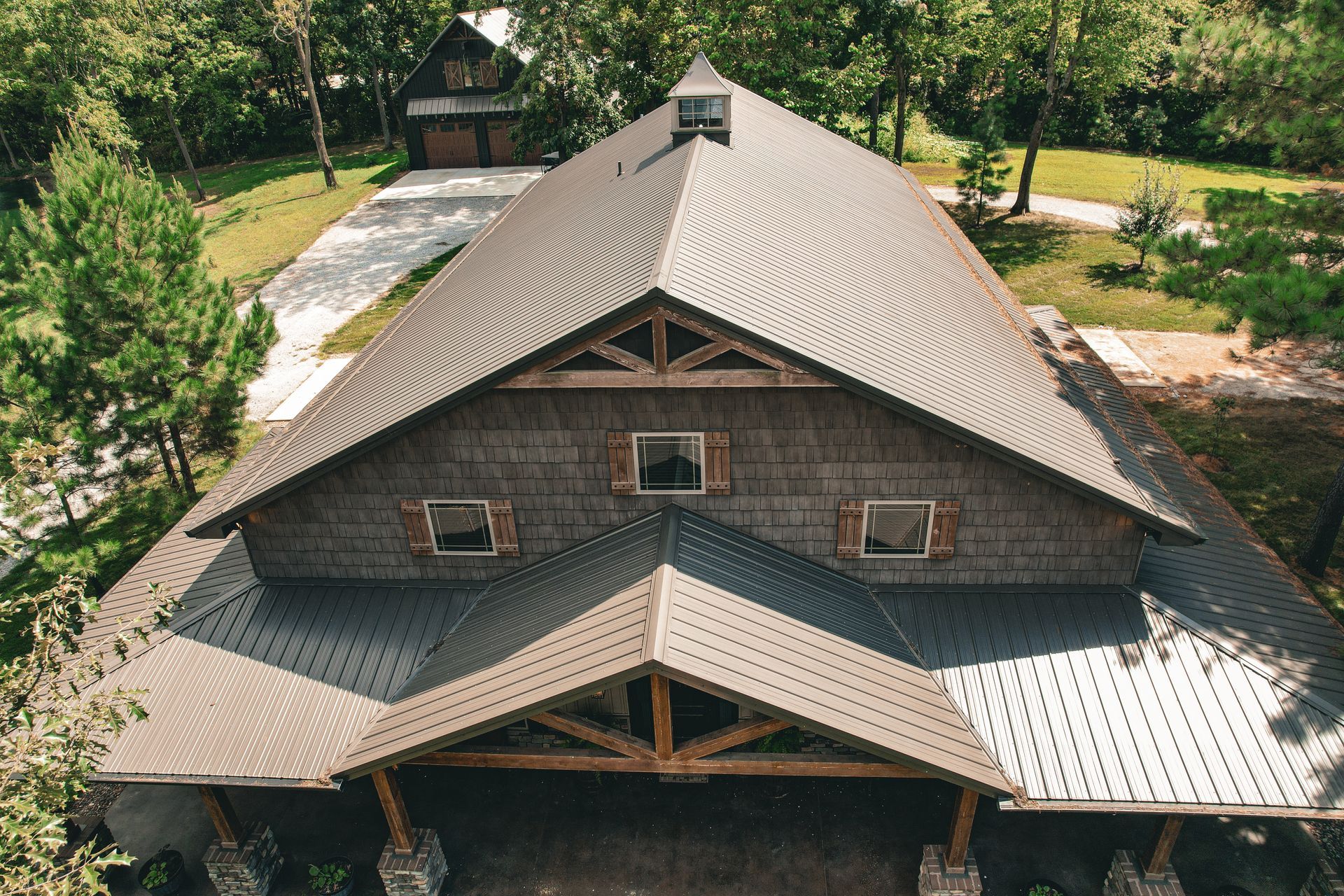 A large barn-like building with a dark roof and wooden facade, set amongst trees, on a bright sunny day.