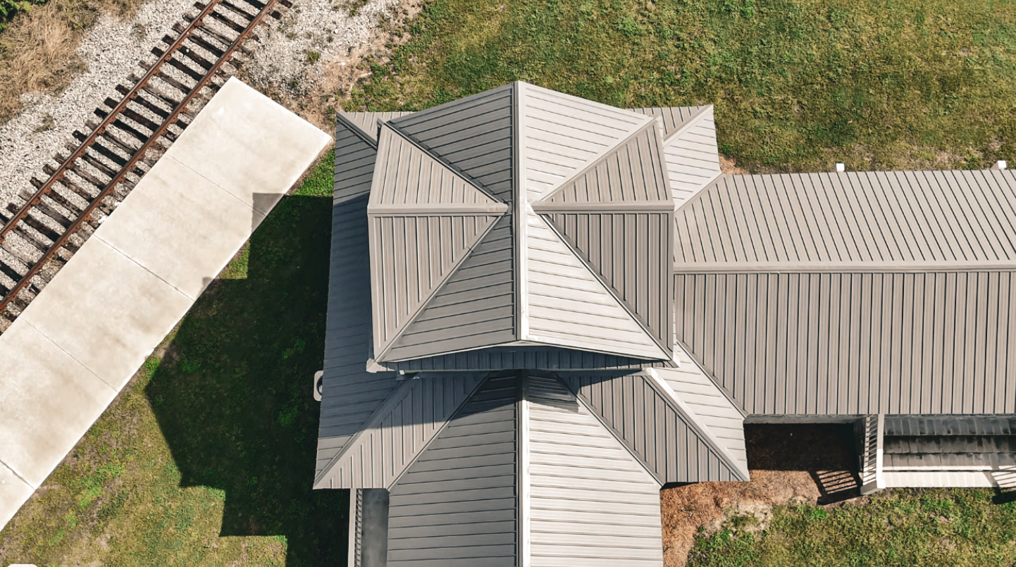 A barn with a green roof and a covered porch in a grassy field.