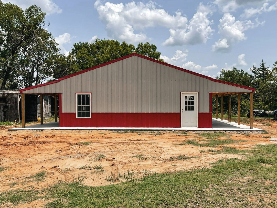 Three-car garage with tan siding, white doors, and a purple metal roof, gravel driveway, sunny day.