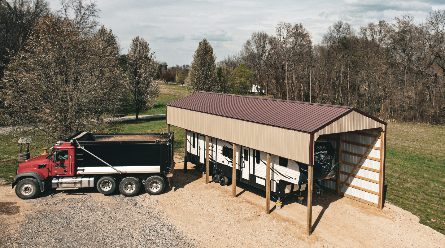 Two-bay metal garage with brown and tan siding and a covered porch on a gravel driveway.