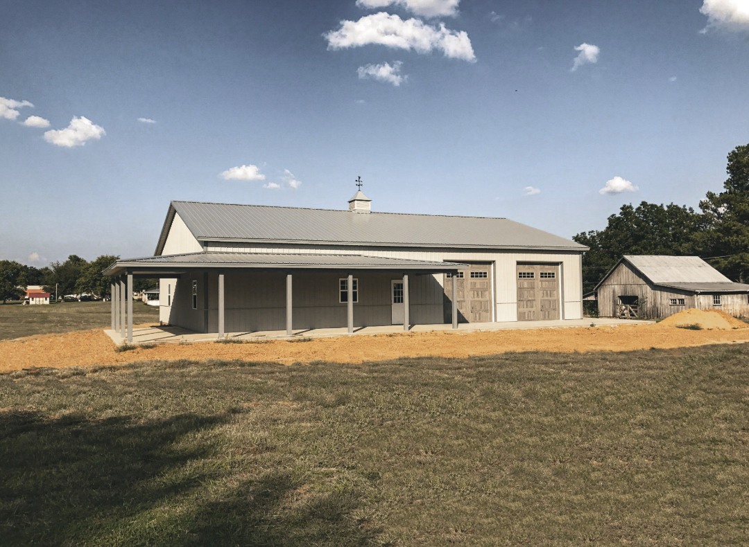 Brown and gray garage with three bays, white doors, and a Jeep parked outside on a dirt lot.