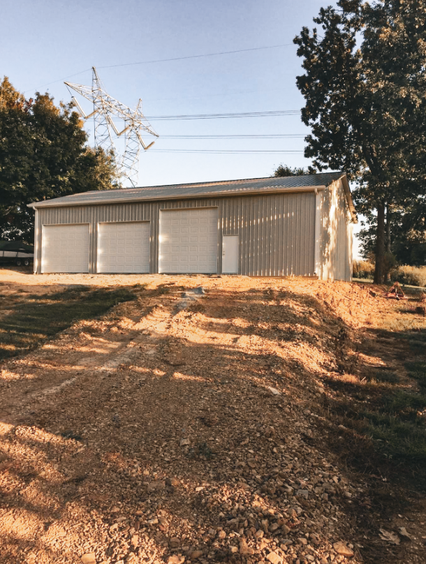 Two-car garage with concrete driveway; gray siding, brown trim; sunset in background.
